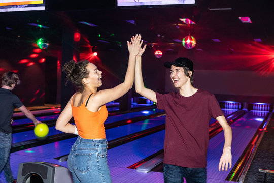 Cheerful friends giving high-five on parquet floor at bowling alley