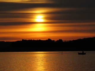 Naklejka premium Sunset Over Beautiful Lake with Boat Silhouette and Cloudy Sky in background