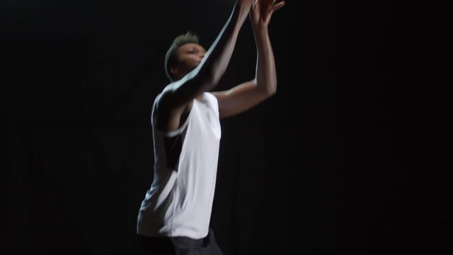 Studio shot of black male athlete catching basketball, then dribbling and shooting it; isolated on dark background
