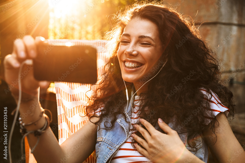 Canvas Prints photo of young european woman 18-20 smiling and speaking on video call via earphones and mobile phon