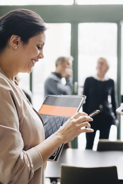 Smiling businesswoman using phone with coworkers in background