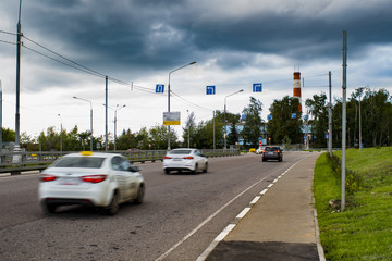 Fototapeta na wymiar Cars taxi drive on city road. Motion blur. Pointers and road signs on cross. Overcast. Storm rain clouds in sky.