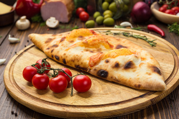 Traditional italian closed pizza Calzone with basil leaves on wooden background