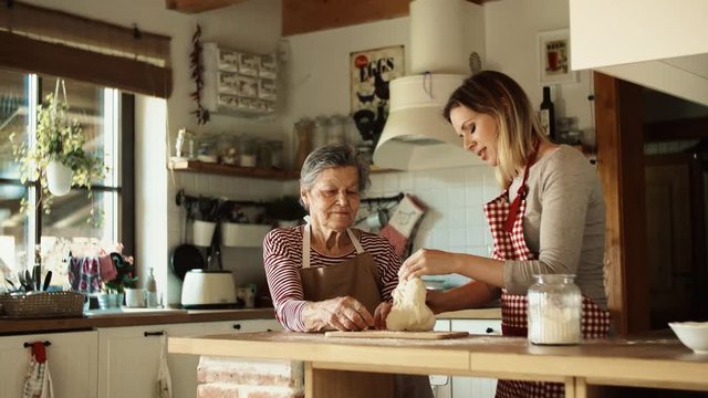 An elderly grandmother with an adult granddaughter making dough at home.