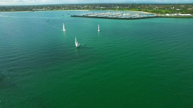 Aerial cinemagram - one sailing sailboat while other frozen with Marina and urban area in the background.