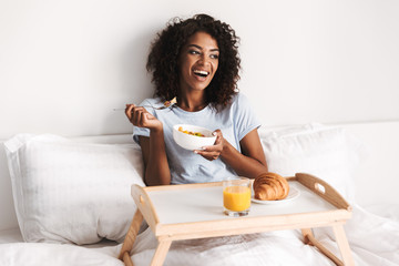 Laughing young african woman having tasty breakfast - obrazy, fototapety, plakaty