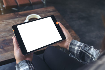 Mockup image of a woman holding black tablet pc with white blank screen with coffee cup on table background