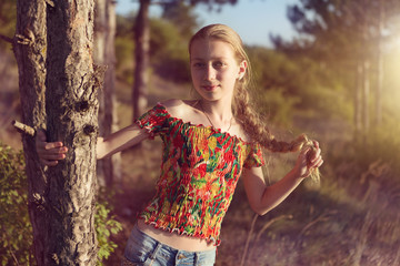 girl in nature, in the forest stands near a pine tree and holds her hand to the trunk of a tree, a girl smiles, emotions and joy, summer, sunbeams