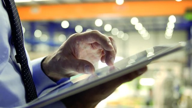 An unrecognizable industrial man engineer standing in a factory, using tablet.