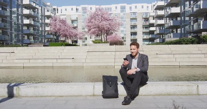 Smartphone - Young urban professional business man using phone relaxing in city. Businessman in 30s using smartphone app in Copenhagen, Denmark, Scandinavia. RED EPIC SLOW MOTION.