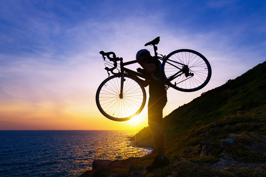 Cyclist man carrying his bicycle standing on the rock at sunset,relaxing concept.