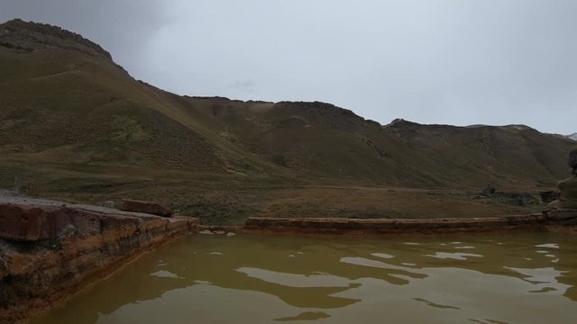 First person scene in hot springs of Cajon Grande in Mendoza, Cuyo, Argentina. Man feet in water and panoramic view of Campanario mountain with snow.Touristic place, natural hot water bath.