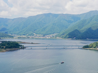 Scenery of Lake Kawaguchi, the biggest lake of Fuji five lakes, with a ferry boat and an overwater bridge crossing the lake and mt Kurodake on the background, famous tourist destination in Japan