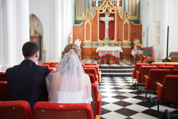 back view of the newlyweds sitting on red chairs of church, selective focus
