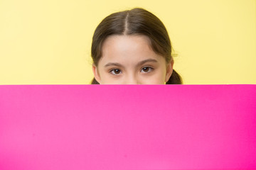 Guess what. Girl kid peeking out pink blank surface copy space. Advertisement concept. Child cute girl brunette looking out of pink paper. Kid cunning face covers secret, close up
