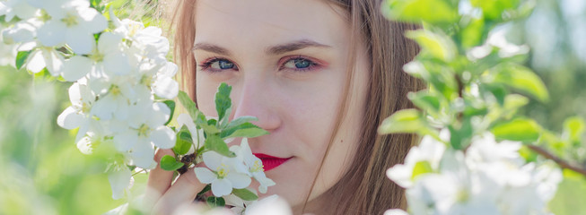 Portrait of a young beautiful woman in white top standing among blooming apple trees on a sunny day. Close-up with space for text.