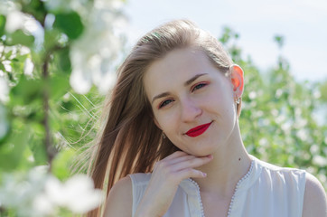 Portrait of a young beautiful woman in white top standing among blooming apple trees on a sunny day. Close-up with space for text.