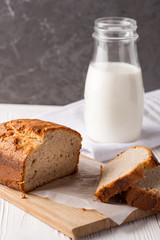 Banana bread in a pan with white parchment paper on a white wooden table with milk bottle in the background. Close up. Bakery concept