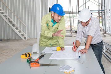 Asian male engineers wear helmet two. he looking at blueprints and talk construction plans analyzing brainstorming, teamwork, meeting concept.