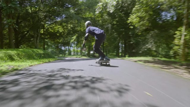 Young man in helmet riding his skateboard very fast and touching the ground in greep park on warm summer day