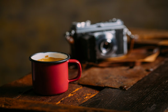 Enamel cup of coffee on a rustic wooden background with a retro camera
