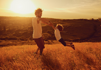 Father and child playing in nature at sunset. Dad throws his son in the park. Fathers day.