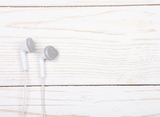 White earbud headphones isolated on a white wooden background with copy space on the right for your text (minimal concept, top view)
