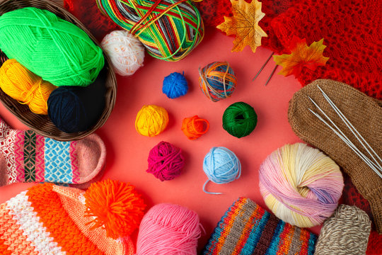Yarn and knitted clothing on a pink background. Orange knitted cap with bubo, colorful yarn, socks, knitting needles are stacked on a pink background. View from above.