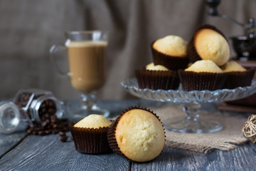 Freshly baked cupcakes on glass dish, cappuccino Cup on wooden surface
