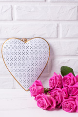 Decorative heart and pink roses flowers on white wooden background against wall.