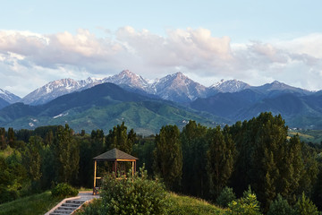 Fototapeta na wymiar Summer houses with benches at evening with at snowy mountains background in dendra park of first president in Almaty, Kazakhstan.