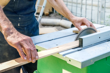 The master sharpens the wooden panel with an electric sander on a Sunny day in the garden.