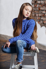 stylish model child. Beautiful teenager girl wearing a blue sweater,jeans,sneakers. Fashion pose model. Young girl sitting chair, looking at camera. Studio shot. series of photos
