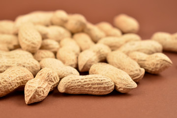 Peanuts on a brown background stock images. Pile of peanuts with nutshell. Roasted Peanuts close up on brown background