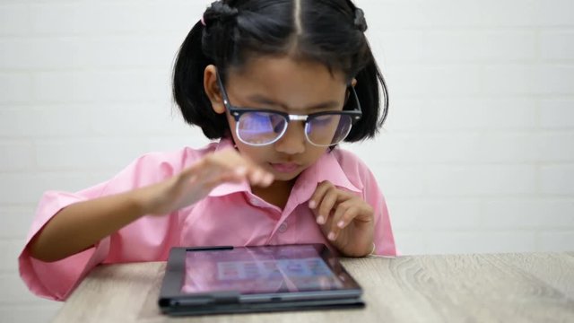 Little girl wear glasses is playing game on teblet