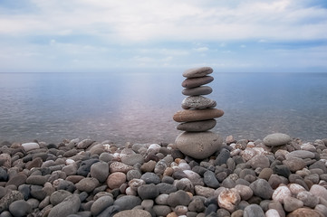 Sea, sky, rocky beach and pyramid of flat gray stones.