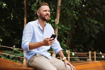 Happy young bearded man outdoors using mobile phone.