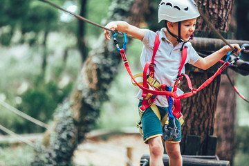 Little boy climbing in adventure activity park with helmet and safety equipment