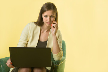 beautiful young girl in a yellow jacket on a yellow background sitting in a chair with a laptop