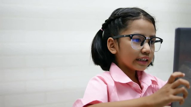 Little girl wear glasses is playing game on teblet with happy