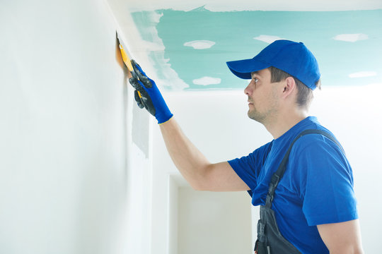 Refurbishment. Worker Spackling A Wall With Putty