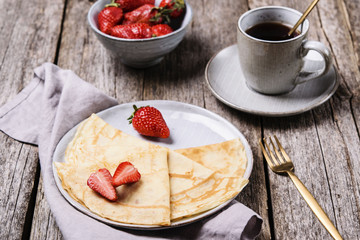 Openwork thin cheese crepes served with strawberry on wooden background. Homemade pancakes. Delicious breakfast