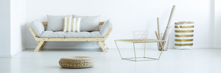Panorama of pouf and gold table in white living room interior with grey wooden sofa. Real photo