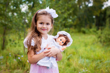 female child in a pink summer dress holding a doll in the hands of