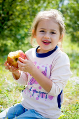 baby girl eating red apple in summer