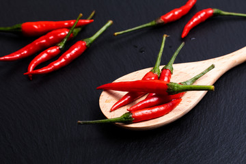 Red Thai chilies pepper in wood spoon on black slate stone background