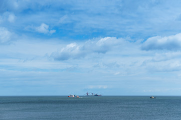 Ships in the sea on the horizon. Oil drilling in the sea. Calm and cloudy sky.