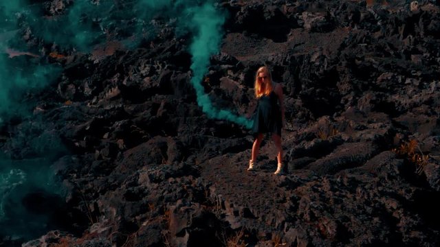 Woman with colored smoke on the volcanic rocky land