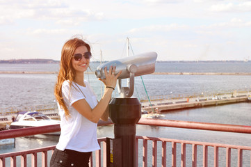beautiful young woman standing on quay near with telescope and smiling.