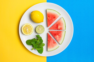 Watermelon on plate with lemon lime and mint leaves on a split color background.